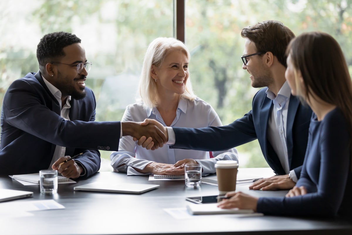 Smiling diverse businesspeople shake hands get acquainted greeting at team meeting in commercial real estate office