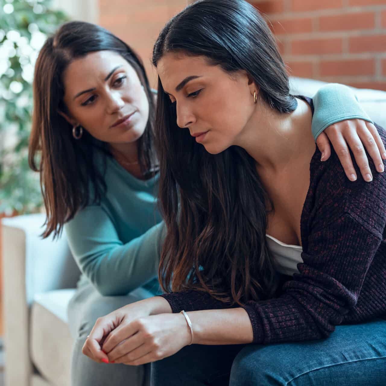 Shot of young woman supporting and comforting her sad friend while sitting on the sofa.